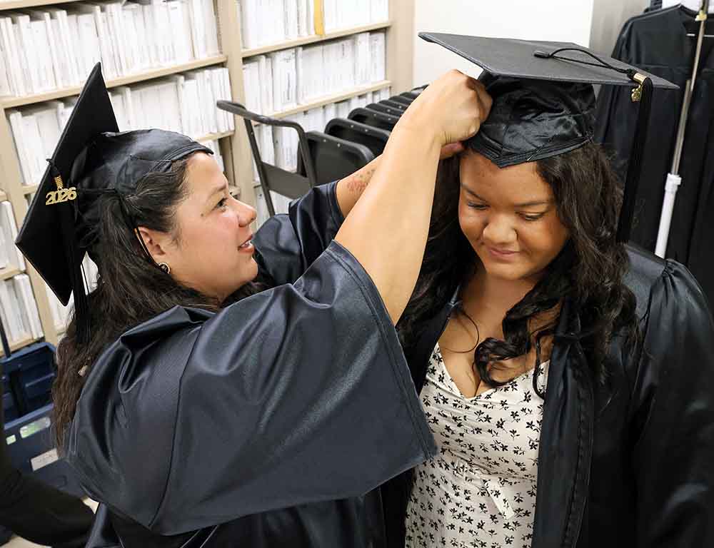 Female graduate helping another graduate pin a mortarboard on her head